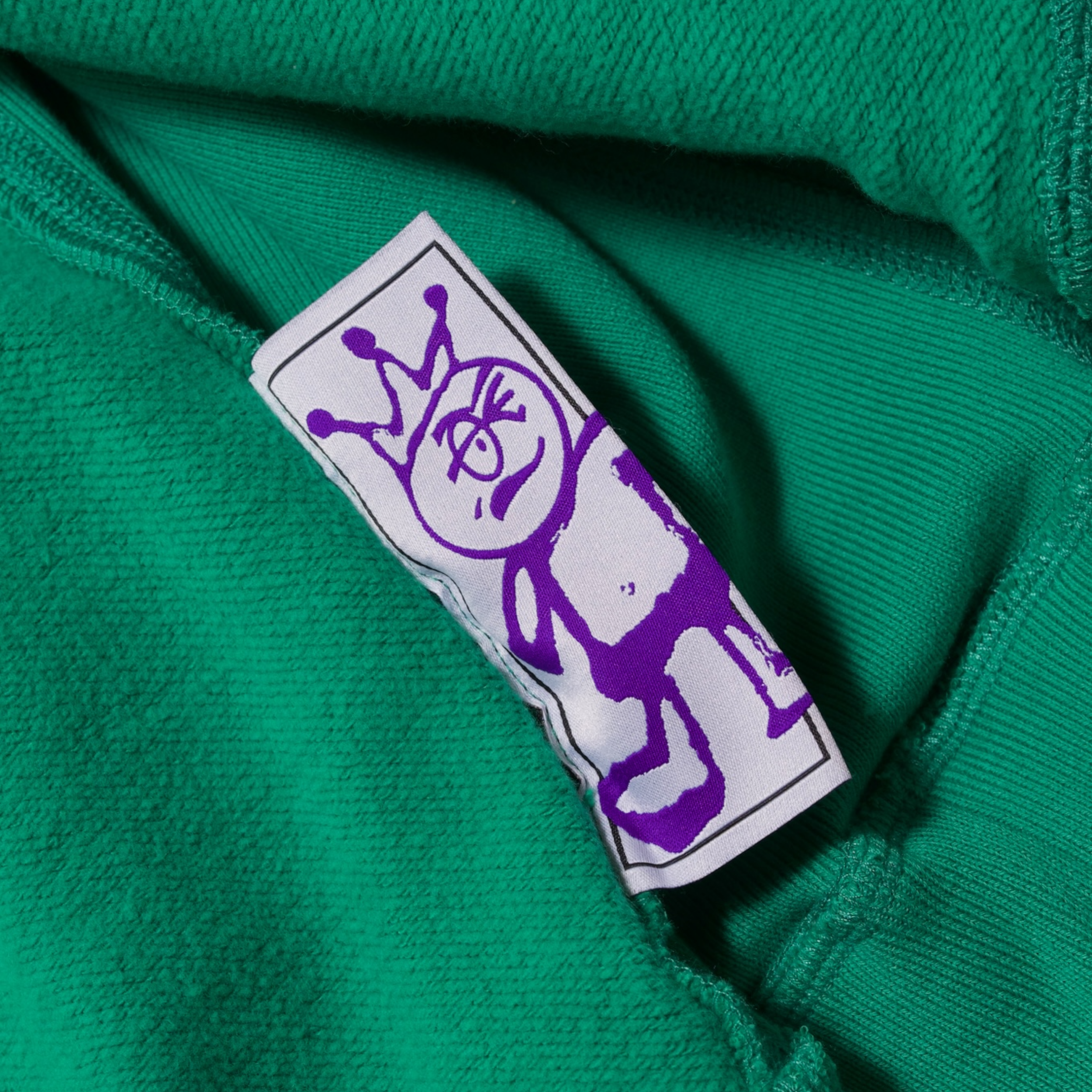 Wash tag for a green hoodie which has a purple character wearing a crown